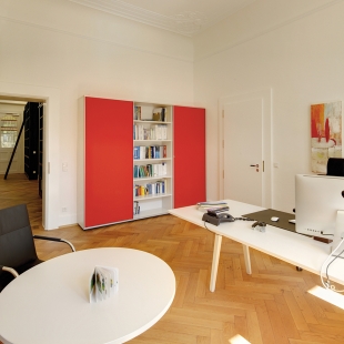 Das flexible Tischsystem Joyn harmoniert mit den großen abschließbaren Schränken, deren Schiebetüren mit farbigem Textil bezogen sind.