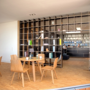 Gleich neben dem Arbeitsbereich befindet sich die Cafeteria. Beide Bereiche wurden mit dem raumhohen Regal FNP optisch voneinander getrennt. Tische und Stühle Maverick aus geölter Eiche harmonieren bestens mit dem Holzboden und der Möblierung.