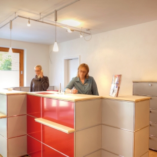 Der großzügige Empfangstresen von USM Haller wurde mehrfarbig gestaltet. Grau und Rot harmonieren perfekt mit den auf Maß gefertigten Holz-Abdeckplatten.